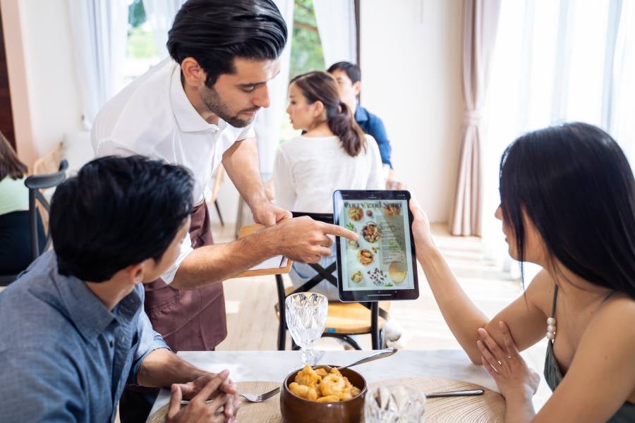 A waiter showing the menu on a tablet to the costumers.