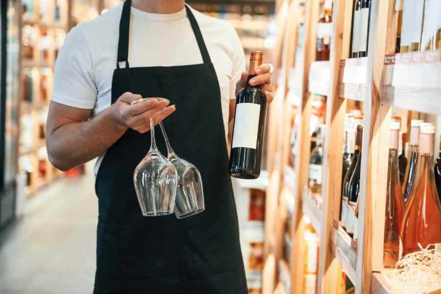 A man holding 2 glasses and a bottle of wine.