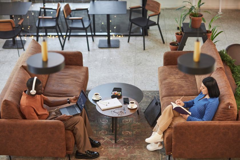 High angle view at two people relaxing on opposite couches in cozy coffee shop enjoying everyday routine copy space.