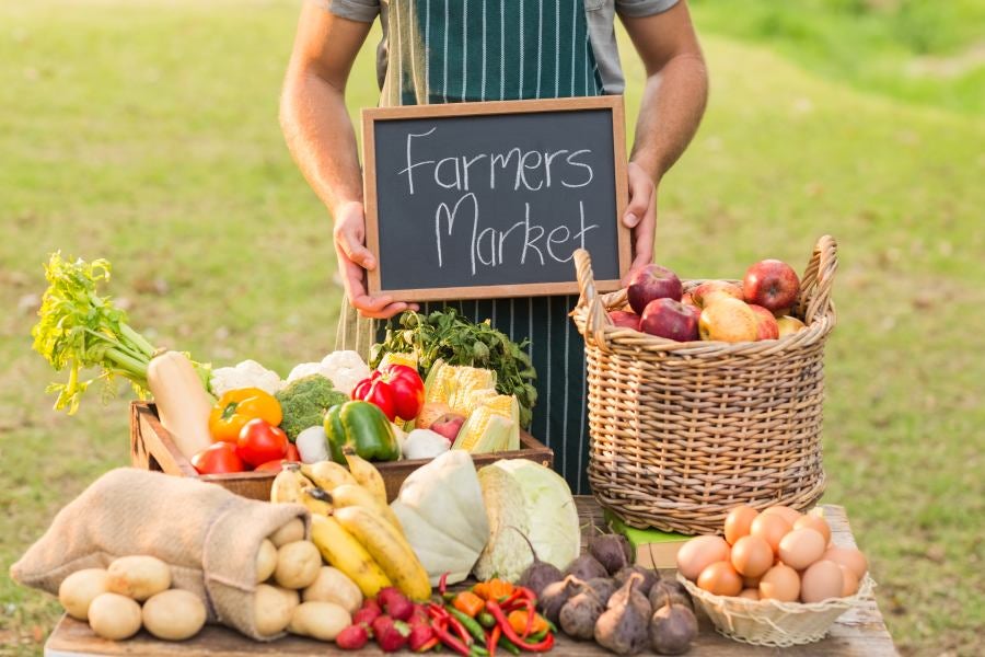 Farmer standing at his stall and holding chalkboard on a sunny day.