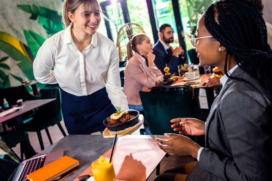 Smiling waitress serving meal to businesswoman in restaurant.