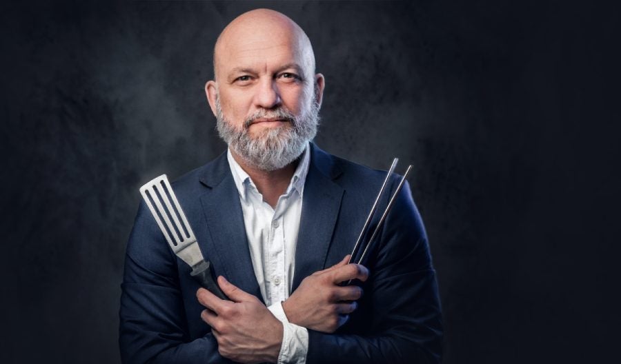 Chef with kitchen spatula and tongs against dark background.