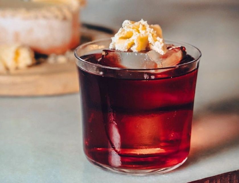 Red cocktail with cheese on top of ice.