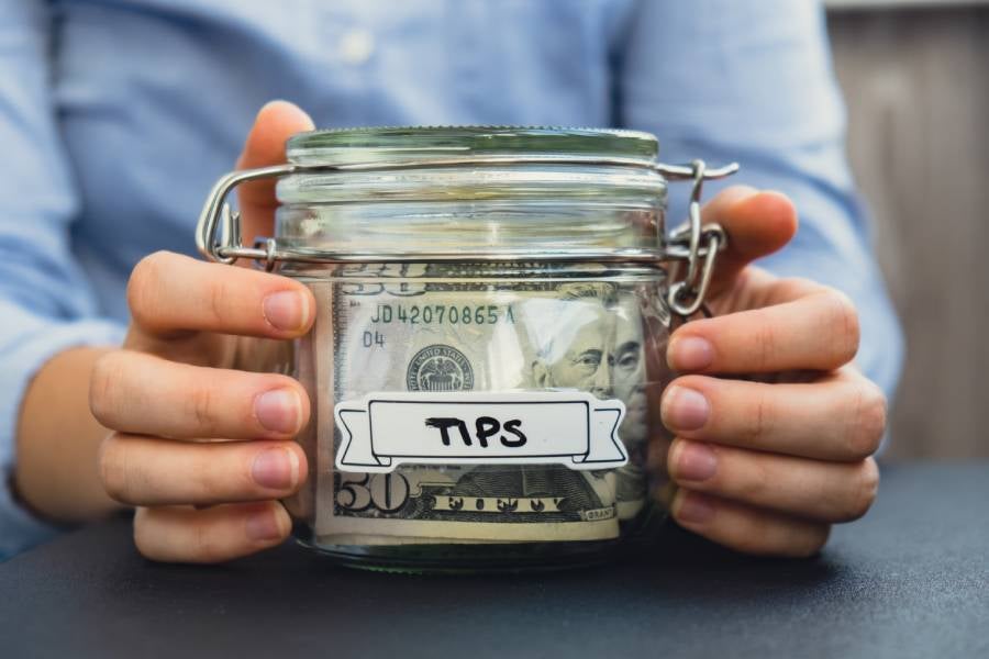 A woman holding a glass jar filled with tips.