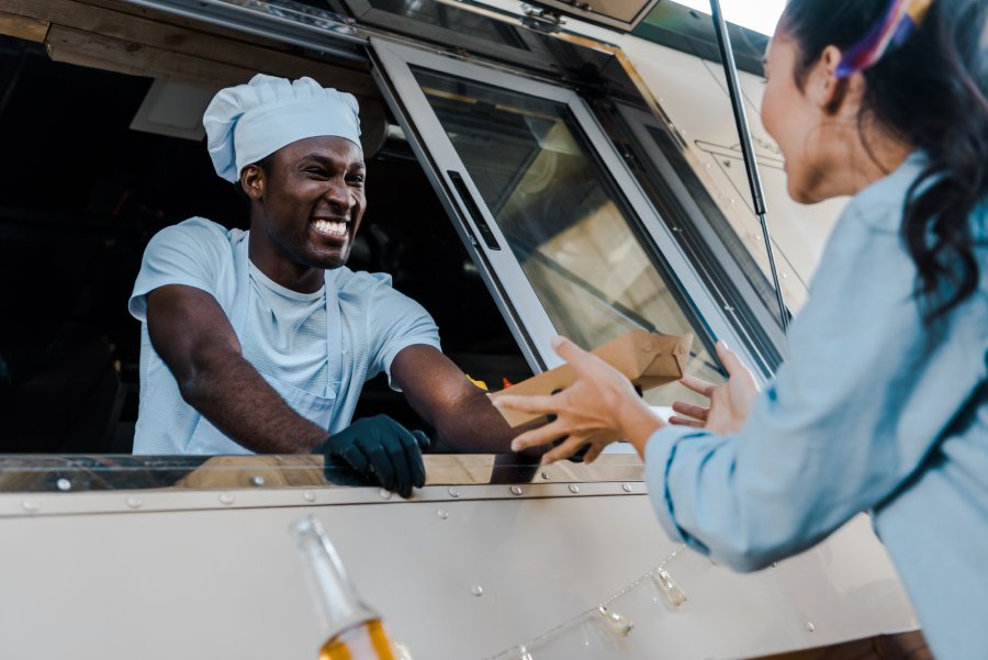 Low angle view of cheerful african american man giving carton plate to customer.